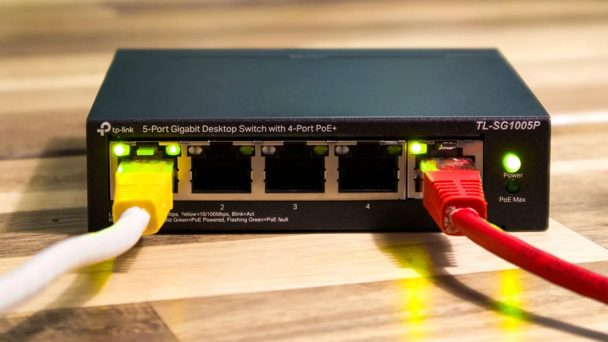 A five port desktop network switch with Power over Ethernet, two Ethernet cables plugged into it and the port lights lit.